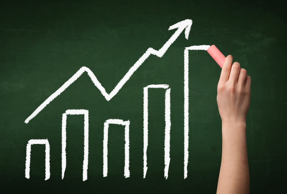 A grown ups hand drawing chart with exponentially growing arrow on green chalkboard